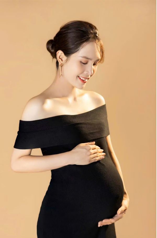 Mẹ bầu mặc đầm đen trễ vai trên nền vàng đồng, phong cách cá tính